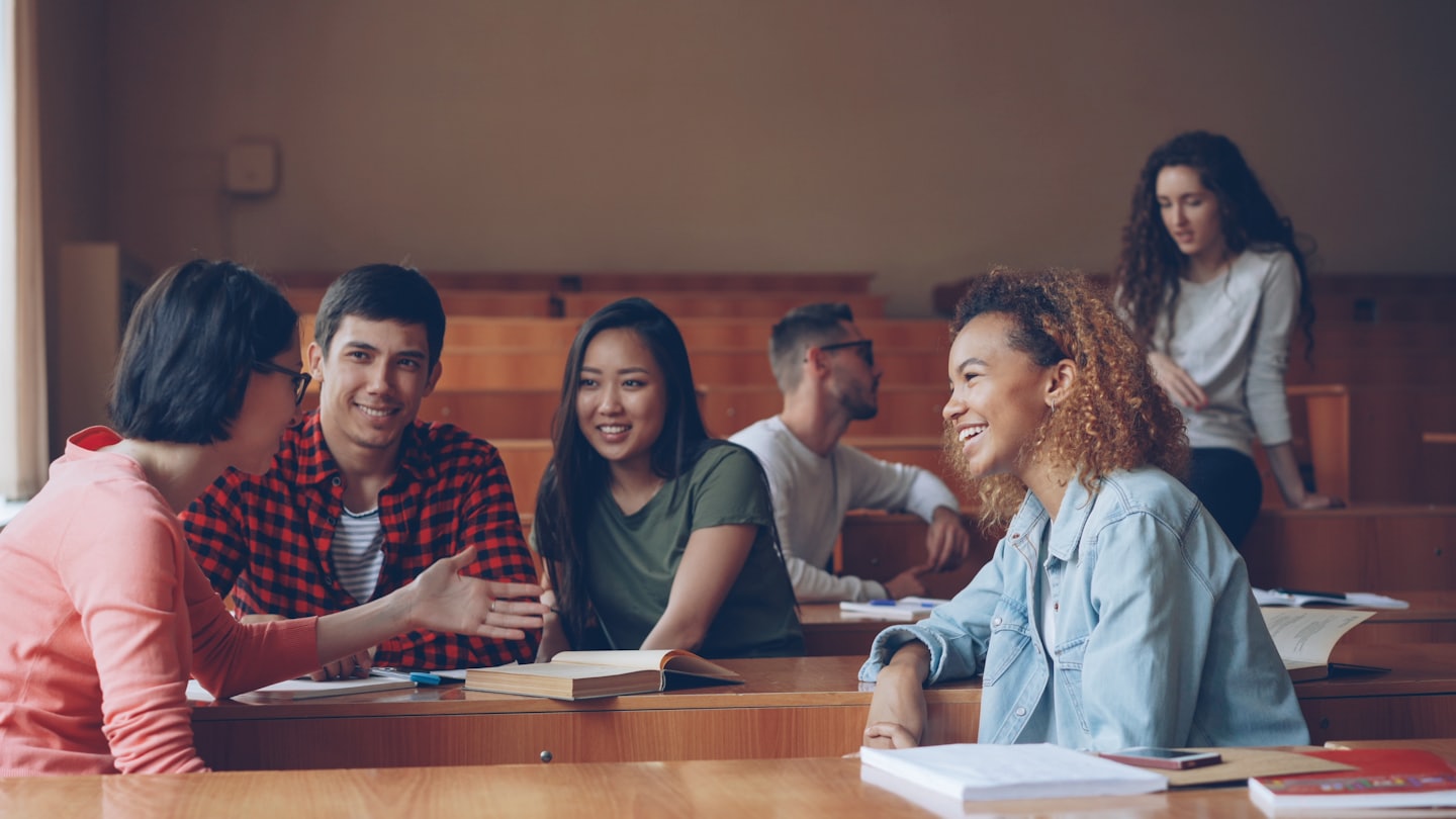 Students laughing and talking together in a lecture hall.
